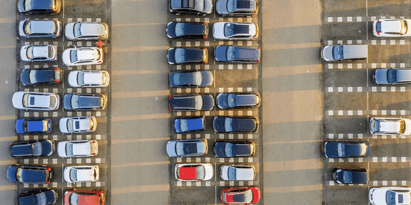 O fotografie aeriană arată multe mașini parcate în rânduri pe o parcare betonată.