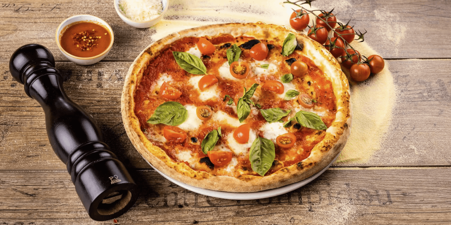 O pizza cu mozzarella, roșii și busuioc lângă piperniță și sos de ardei iute.