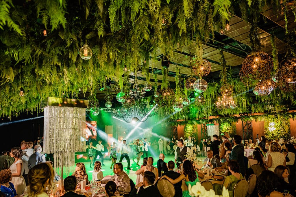 Petrecere cu oameni, dansatori pe scenă și un tavan verde decorat cu lumini și oglinzi.