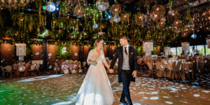 Un cuplu proaspăt căsătorit se ține de mână pe ringul de dans la o nuntă, cu discoboluri.