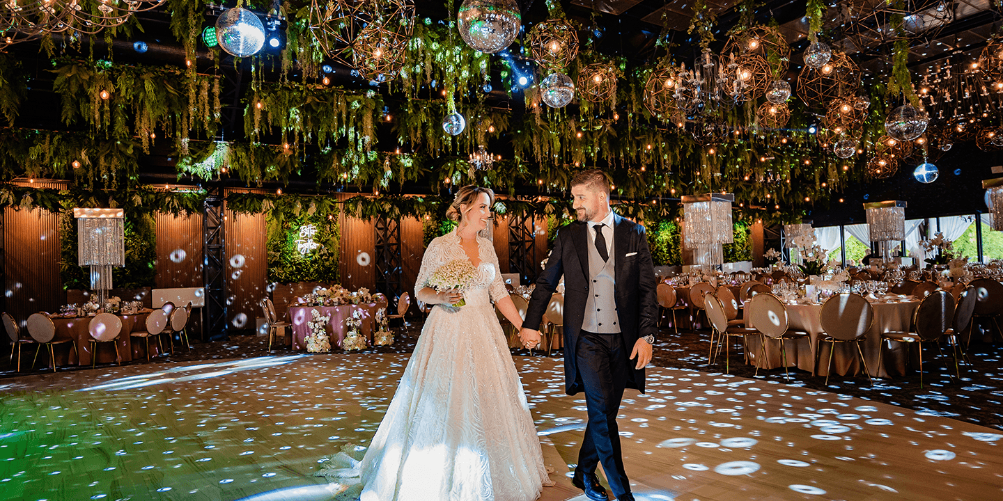 Un cuplu proaspăt căsătorit se ține de mână pe ringul de dans la o nuntă, cu discoboluri.