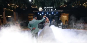 Un cuplu dansează la Domeniile Șahtica. Mireasa poartă o rochie albă și mirele un costum verde deschis.