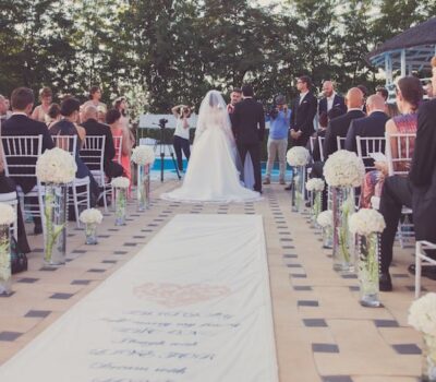 O ceremonie de nuntă în aer liber cu o mireasă, mire, invitați și decorațiuni florale.