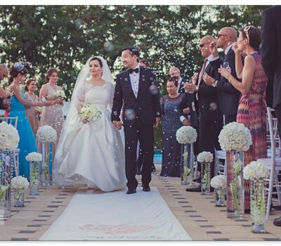 Un cuplu de proaspăt căsătoriți merg pe culoarul unei nunți, în timp ce oaspeții suflă bule.