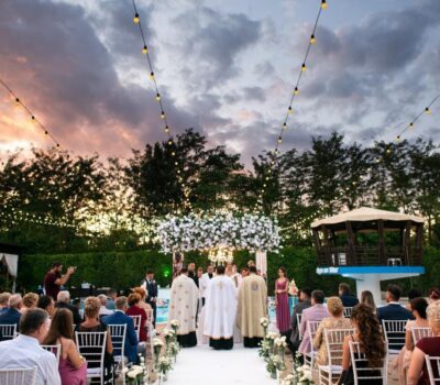 Oamenii participă la o ceremonie de nuntă în aer liber, cu lumini de sărbătoare atârnate deasupra.