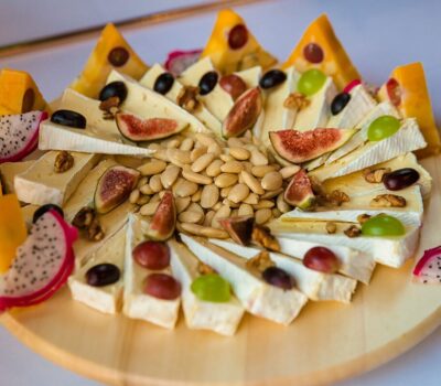 Un plat din lemn plin cu brânză brie feliată, brânză cheddar, smochine proaspete, nuci și fructe dragon.