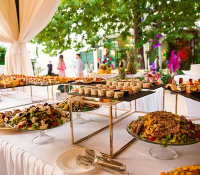 Masa de bufet cu diverse aperitive, salate și decorațiuni la un eveniment exterior.