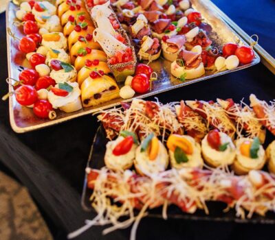 Două platouri cu aperitive asortate, cu roșii cherry, brânză și carne.