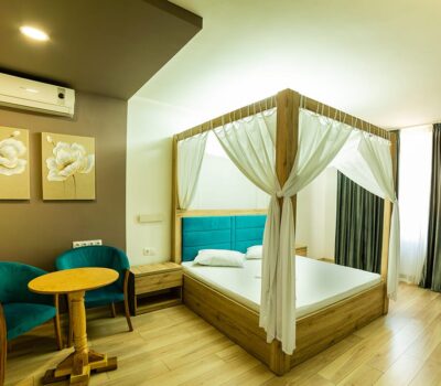 Interior modern al camerei cu pat cu baldachin, scaune turcoaz, podea din lemn și opere de artă florale.