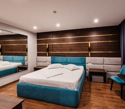 Un dormitor luxos cu un pat matrimonial albastru, noptiere și un perete cu panouri din lemn.