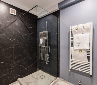 O cabină de duș are pereți cu aspect de marmură neagră, un paravan de sticlă și un suport alb pentru prosoape.