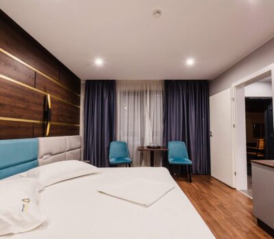 Interior de cameră de hotel cu pat dublu, pereți din lemn, scaune turcoaz și TV.