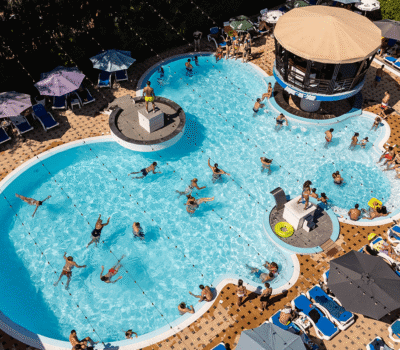 Vedere aeriană a unei piscine aglomerate cu oameni, șezlonguri și umbrele de soare.