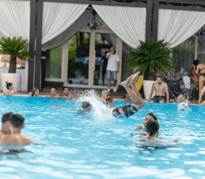 Oamenii se bucură de o piscină cu copaci și perdele albe în fundal.