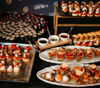 O masă cu mai multe farfurii cu gustări, inclusiv sushi, bruschete și sosuri.