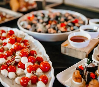 Mese cu aperitive variate: frigărui cu roșii și mozzarella, salată, sushi și boluri cu sosuri.