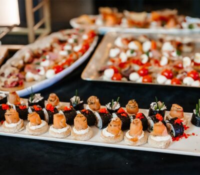 Aperitive cu sushi, roșii și mozzarella pe platouri albe.