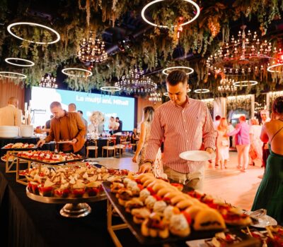 Bufet cu aperitive la evenimentul "La mulți ani, Mihail", iluminat festiv, și invitați îmbrăcați elegant.