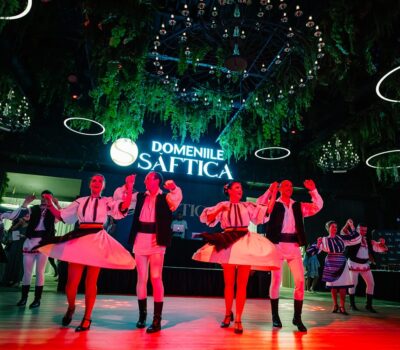 Grup de dansatori în costume populare la Domeniile Știrbey, sub lumini și decorațiuni verzi.