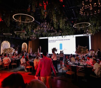 Interior somptuos decorat pentru eveniment, cu ecran mare. Text: "Ce aplicație preferă Mihai la birou?".