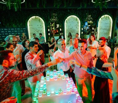 Un grup de oameni sărbătoresc cu shot-uri într-un bar cu pereți acoperiți de plante.