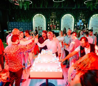 Un grup de oameni care sărbătoresc cu o tortă realizată din pahare cu băuturi.