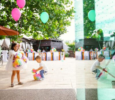 O fetiță și un băiat cu baloane și jucării de pluș curcubeu la o petrecere în aer liber.