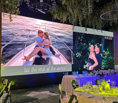 Interiorul unei săli de nunți arată un ecran LED cu cuplul Sergiu și Iasemina și mese decorate.