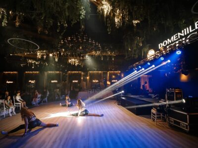 Trei dansatoare fac șpagatul la Domeniile Saga, sub lumini și un candelabru.