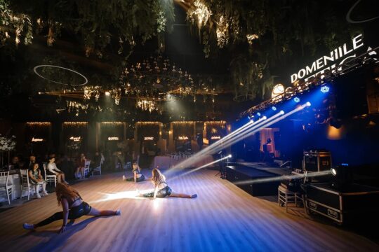 Trei dansatoare fac șpagatul la Domeniile Saga, sub lumini și un candelabru.