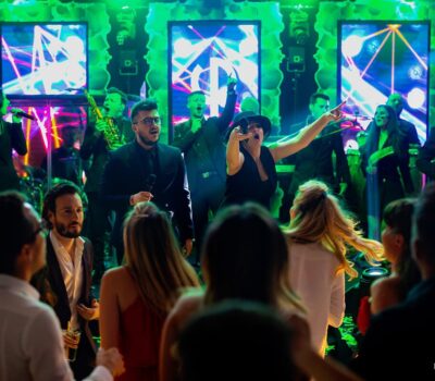 O trupă live interpretează în fața unei mulțimi la un eveniment, lumini verzi strălucind în fundal.