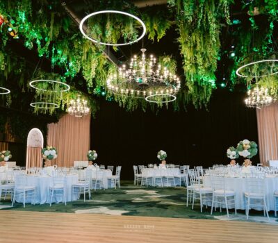 O sală de evenimente împodobită cu candelabre, verdeață, mese rotunde și scaune albe.