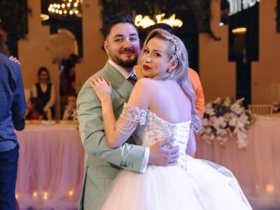 Un cuplu îmbrățișat, el cu costum verde pal, ea cu rochie albă la eveniment.