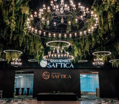 Interiorul luxos al Domeniilor Șaftica, cu candelabre, verdeață și logo-ul „Domeniile Șaftica”.