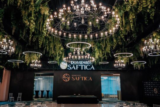 Interiorul luxos al Domeniilor Șaftica, cu candelabre, verdeață și logo-ul „Domeniile Șaftica”.