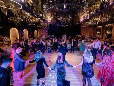 Într-o sală de bal împodobită, o adunare bucuroasă dansează, ținându-se de mână într-un cerc. Muzicienii cântă.