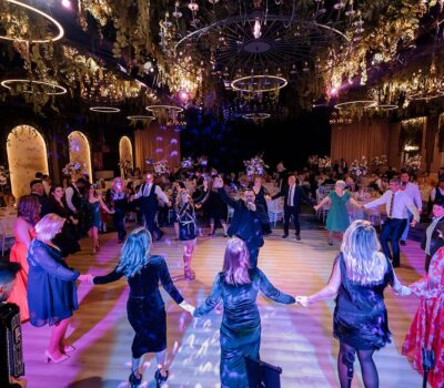 Într-o sală de bal împodobită, o adunare bucuroasă dansează, ținându-se de mână într-un cerc. Muzicienii cântă.