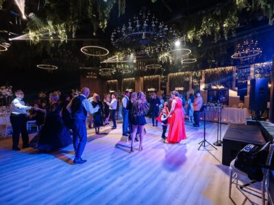 Oameni care dansează într-o sală de bal cu candelabre și lumini de scenă.