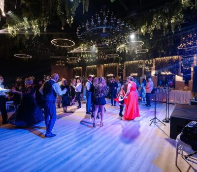 Oameni care dansează într-o sală de bal cu candelabre și lumini de scenă.