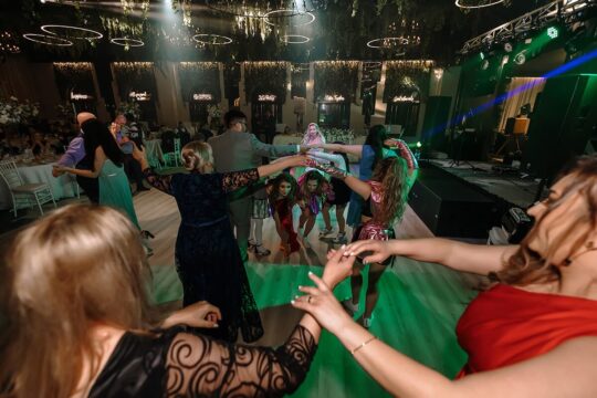 Un grup de oameni formează un cerc, cu mâinile împreunate, într-o cameră frumos decorată.