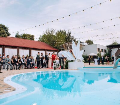 Nunta în aer liber lângă piscină, oaspeții așezați, cuplul în picioare, fotograf care face poze.