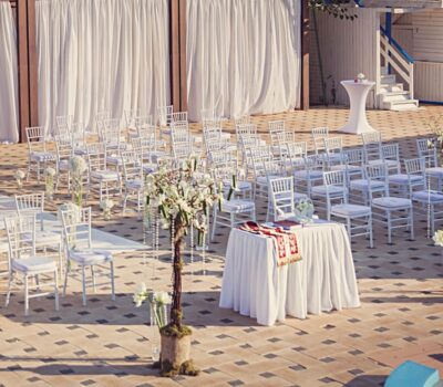 Configurare nuntă în aer liber cu scaune albe, draperii și un altar cu flori.