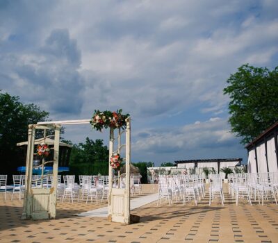 Ceremonie de nuntă în aer liber, cu scaune albe și o arcadă florală unică realizată din uși vintage.