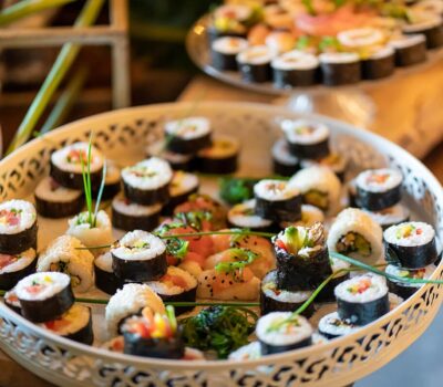 Un sortiment de sushi într-un bol alb decorativ și o farfurie cu mai mult sushi în fundal.