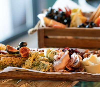 Un aranjament de aperitive cu brânză, nuci și fructe pe o tavă de lemn și o ladă.