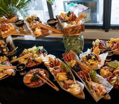 Platouri cu brânzeturi și mezeluri, pe o masă cu față de masă neagră.