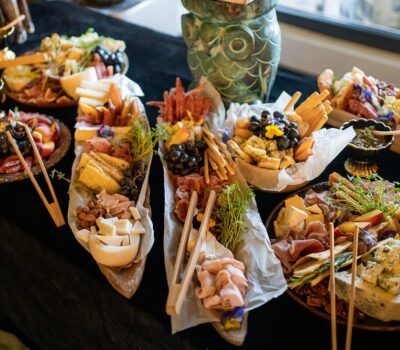 Aranjament de mâncare cu brânză, carne și fructe pe farfurii și planșe de lemn pe o masă neagră.