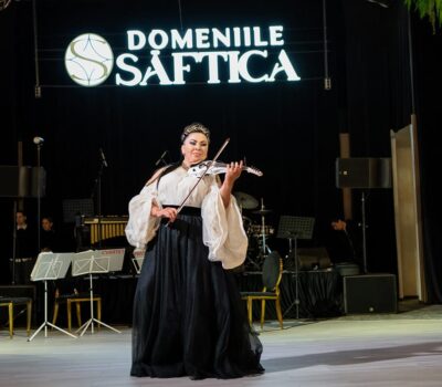 O femeie cântă la vioară pe scenă, sub sigla Domeniile Șăftica.