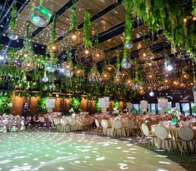 Interior împodobit cu plante verzi atârnate, lumini geometrice și bile de discoteca deasupra meselor rotunde cu fețe de masă bej.