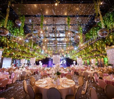 O sală de evenimente decorată cu verdeață, luminișoare și sfere disco, cu mese rotunde aranjate.